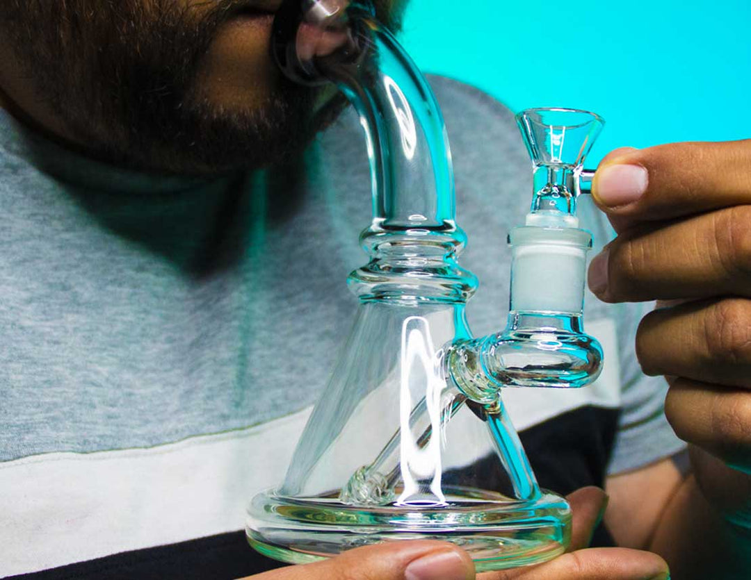 Man holding Glass Waterpipe in studio with blue and green lighting.